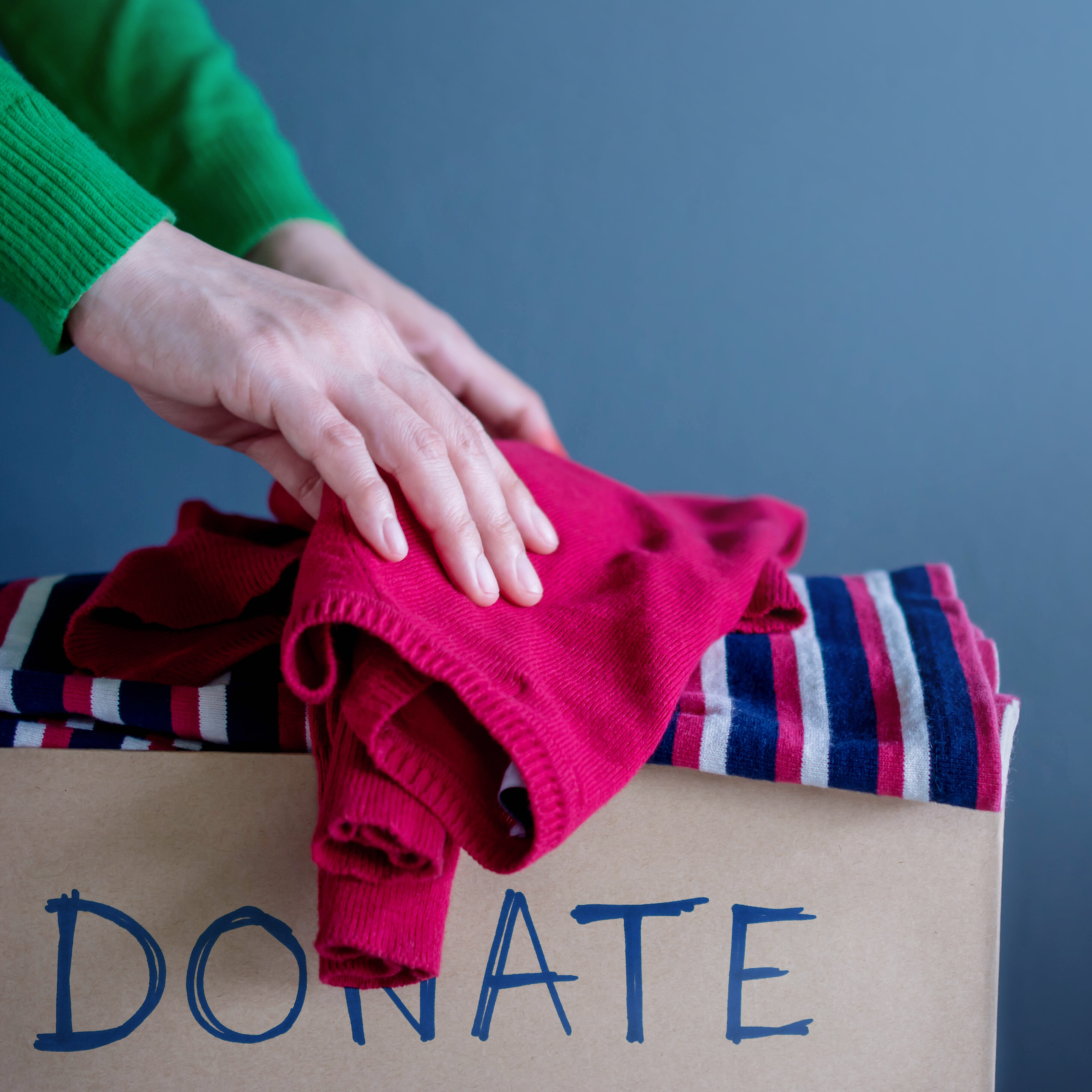 Hands holding clothing over a cardboard box labeled donate