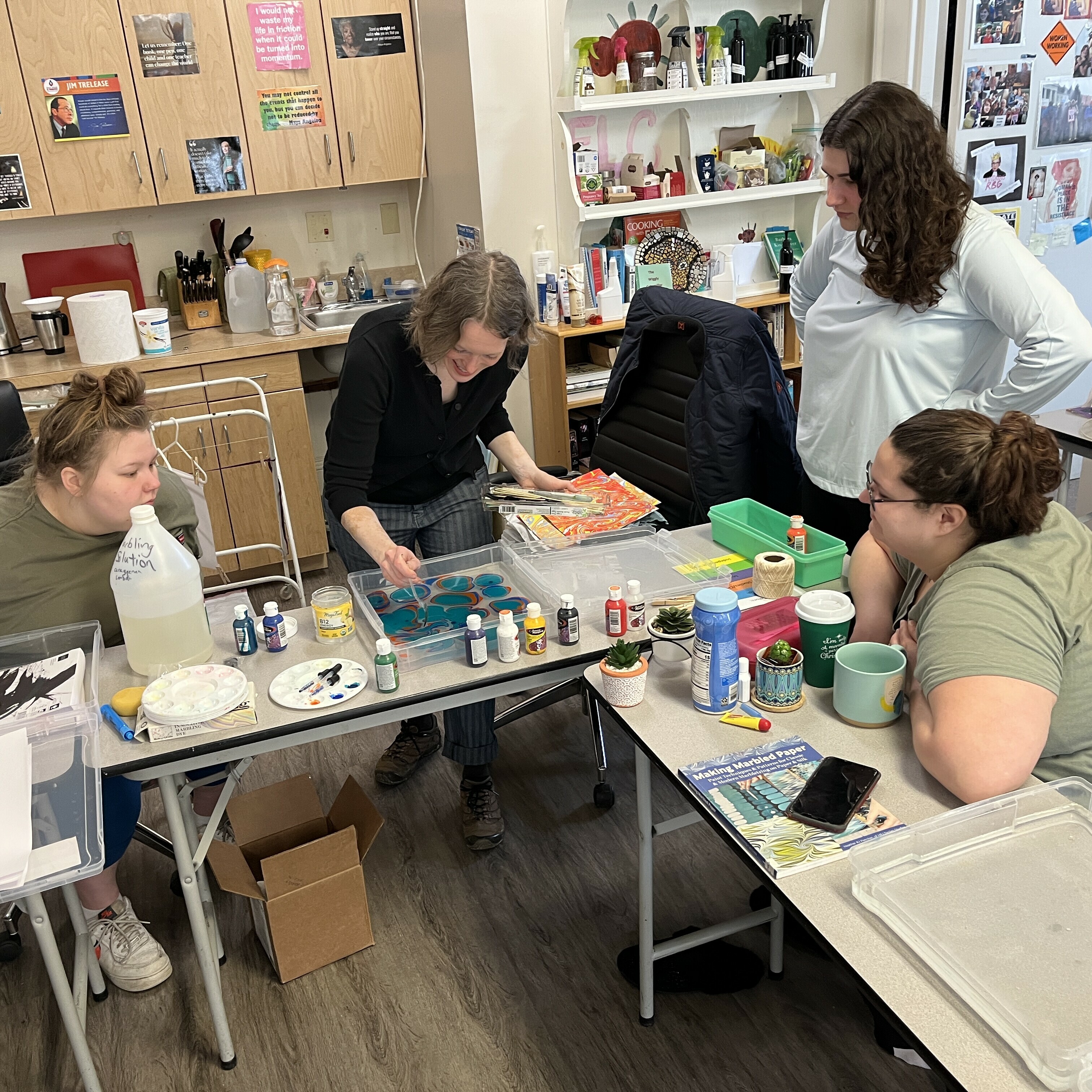 Four people engaged in an art activity, surrounded by paints, brushes, and supplies.