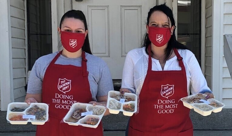 Two masked women holding prepared meal trays