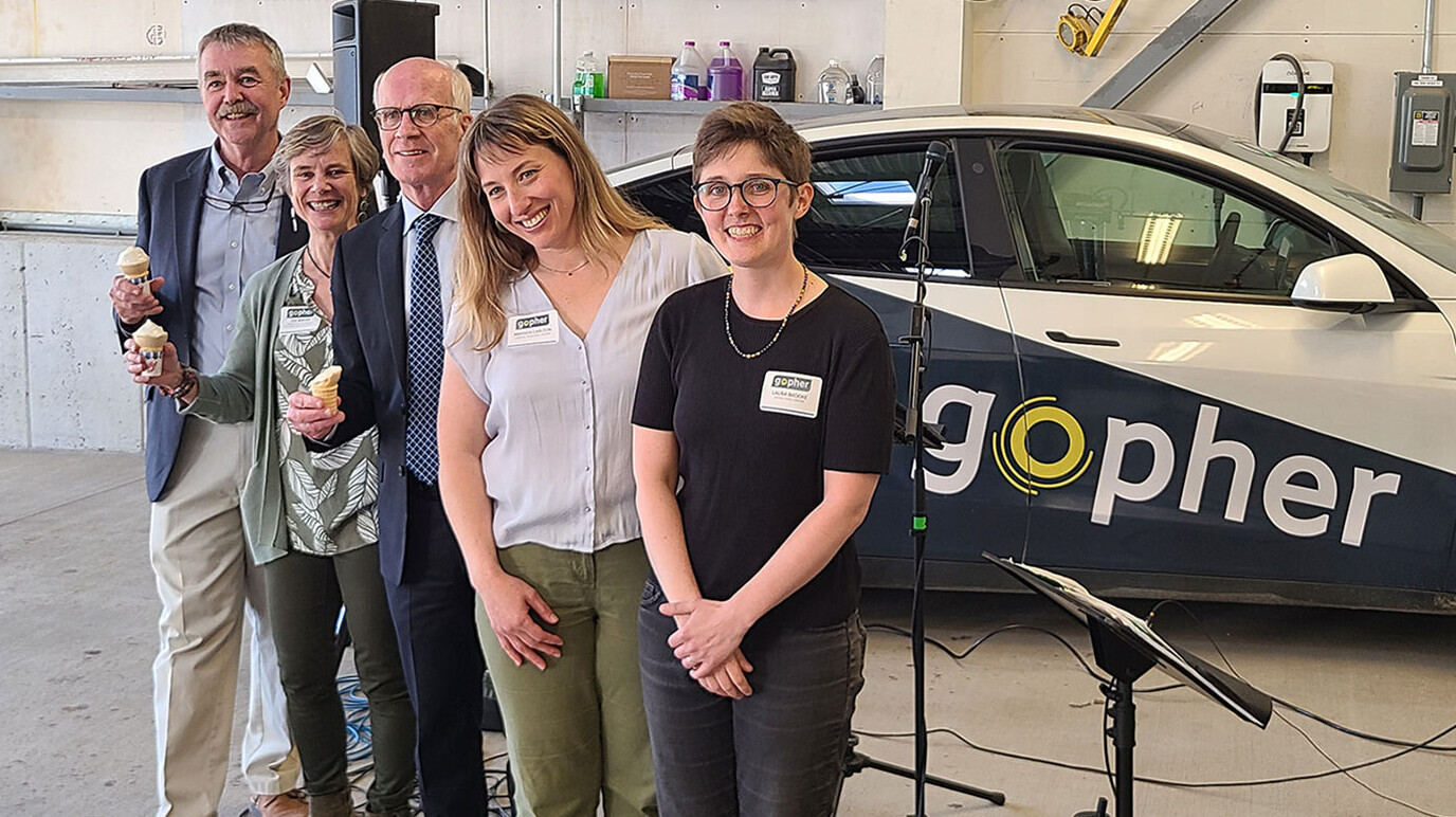 Smiling group poses in front of Gopher electric car