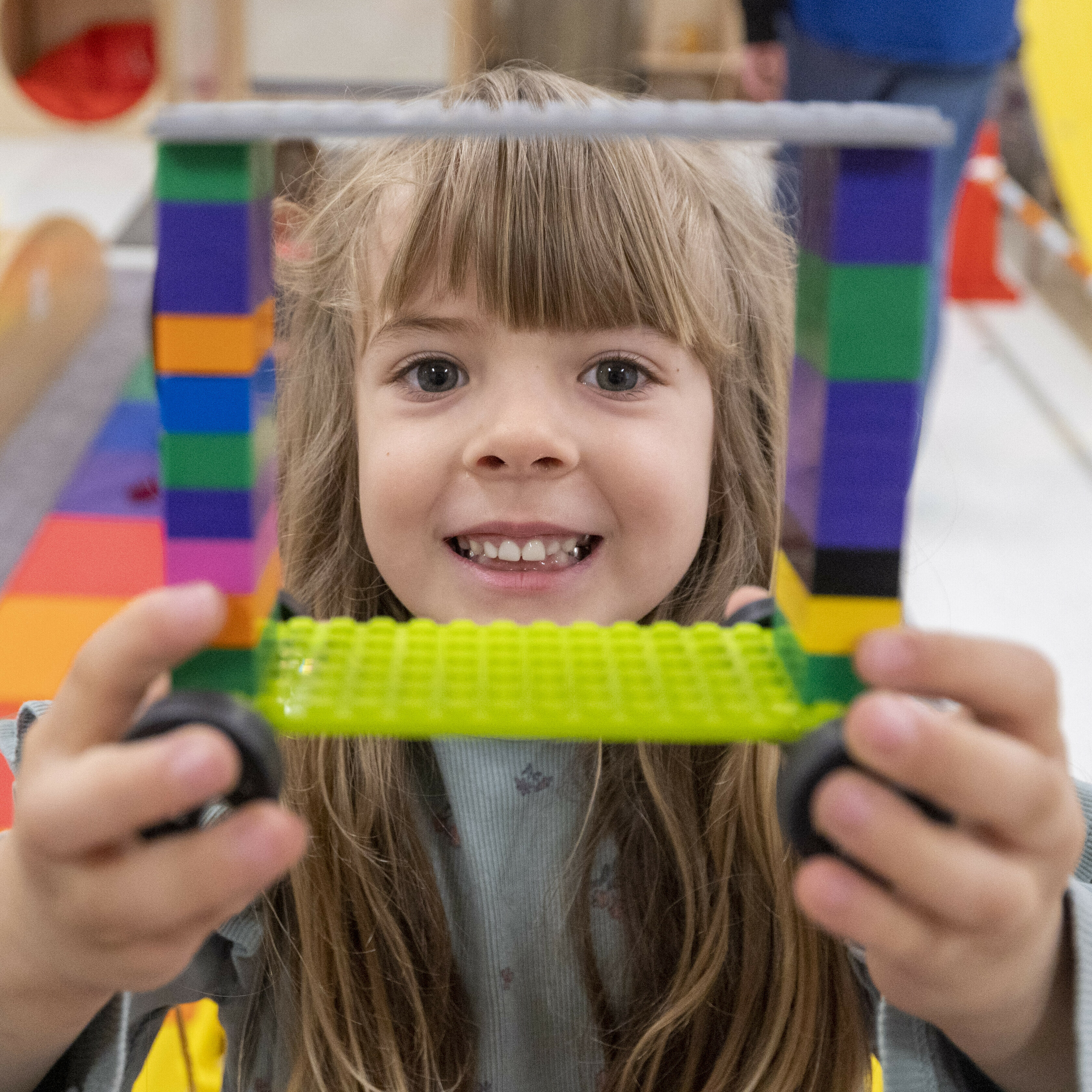 Girl smiling and holding a colorful LEGO creation with wheels.