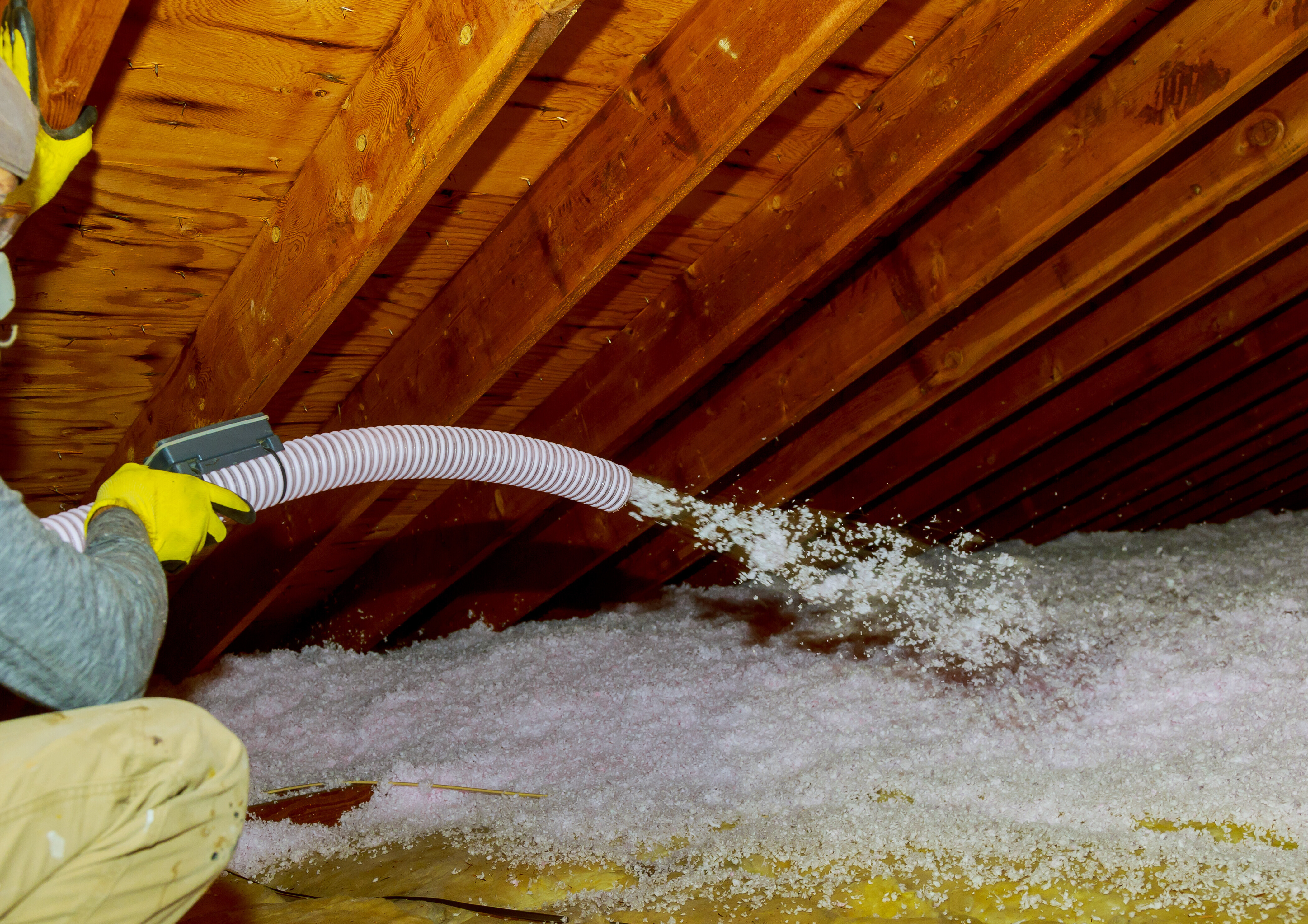 A person in an attic holding a hose for blow in insulation