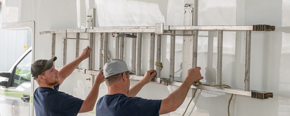 Two men placing a ladder on the side of a truck