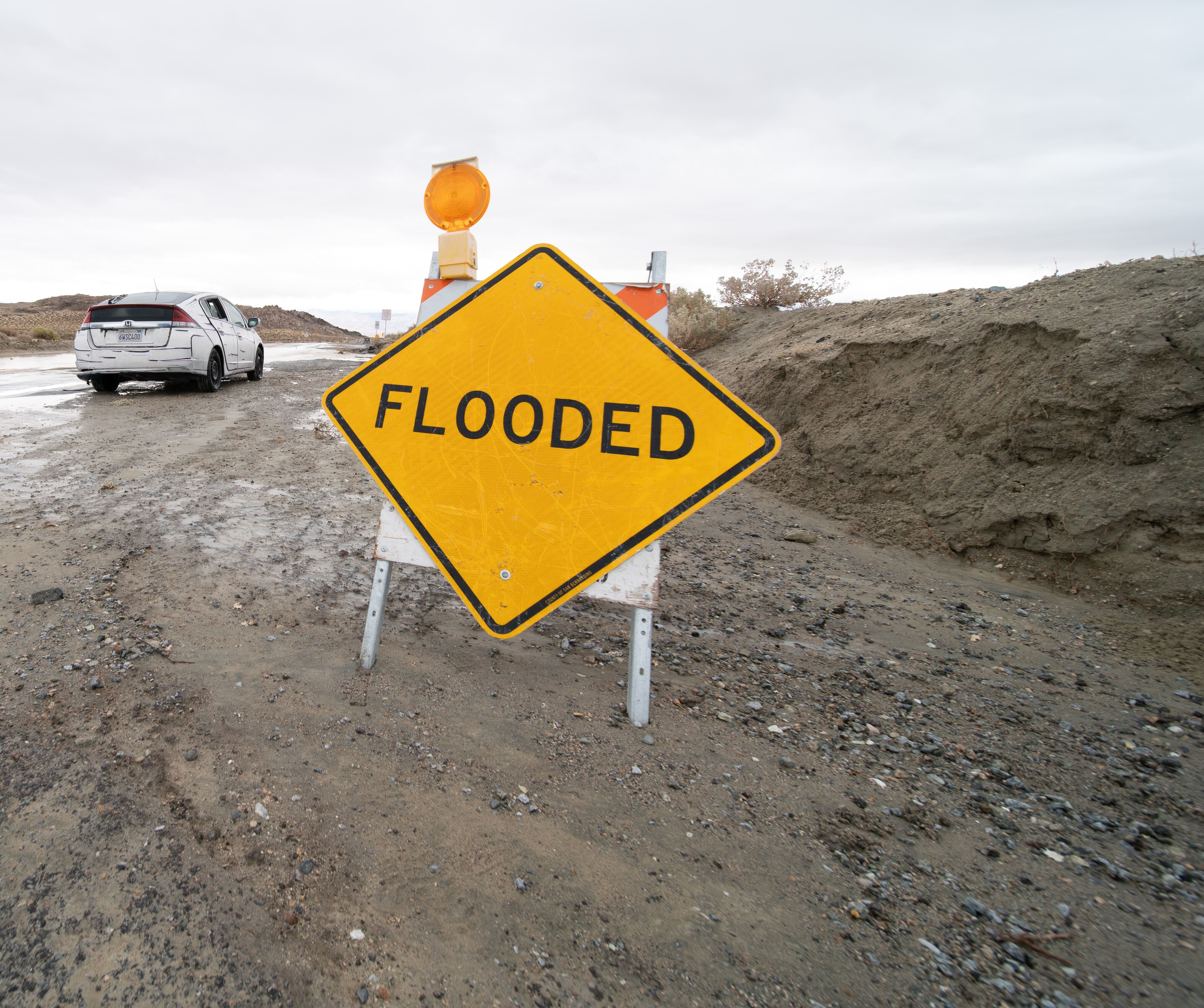 A caution sign stating Flooded on the side of a dirt road