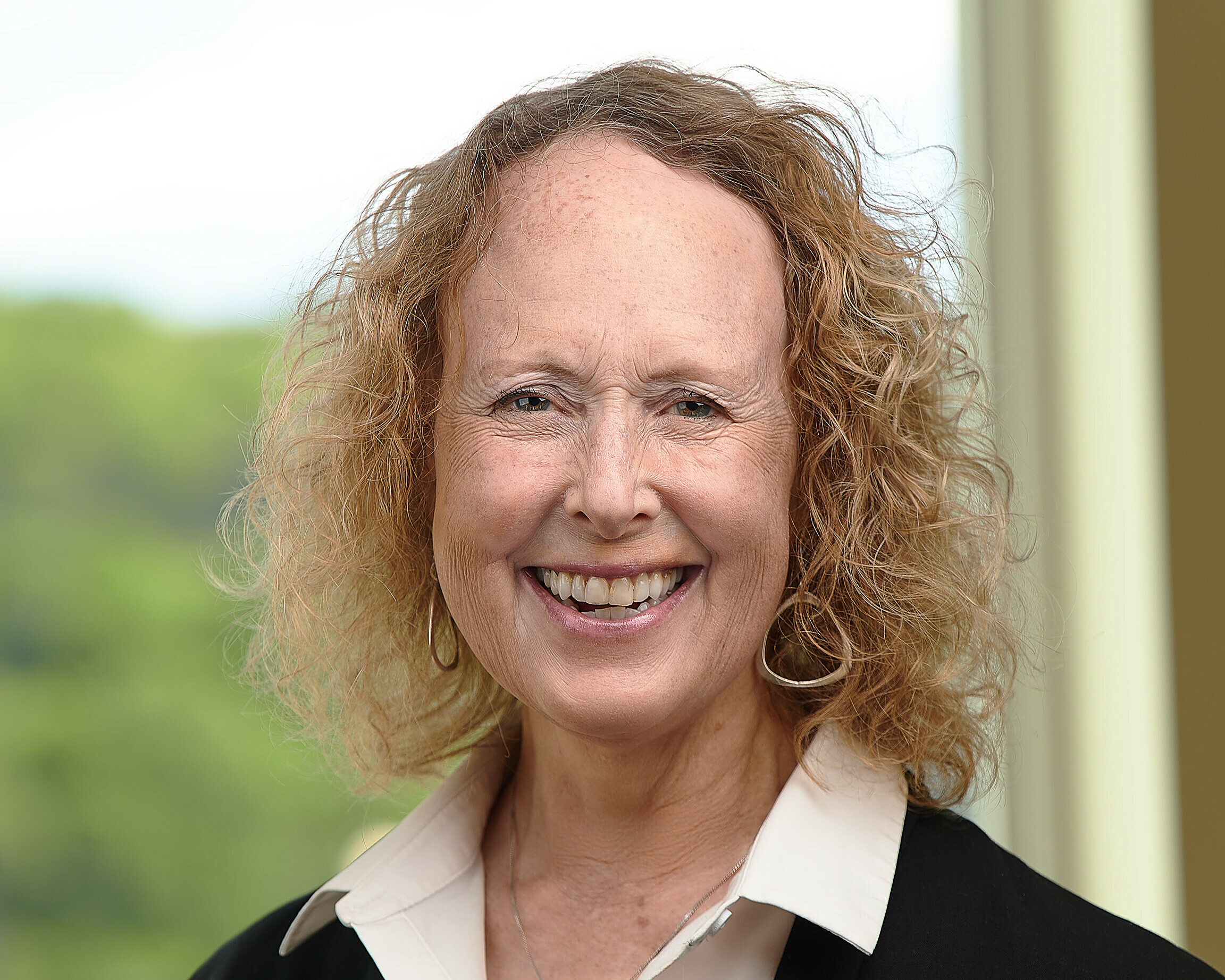 Smiling woman with curly hair, wearing a black jacket and white shirt.