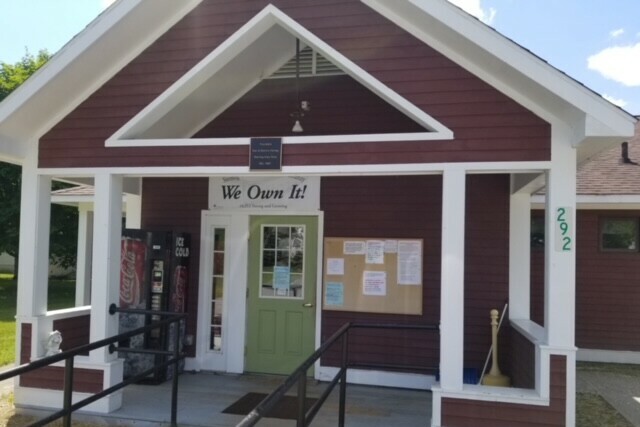 Front of a red building with a green door, featuring a sign reading 