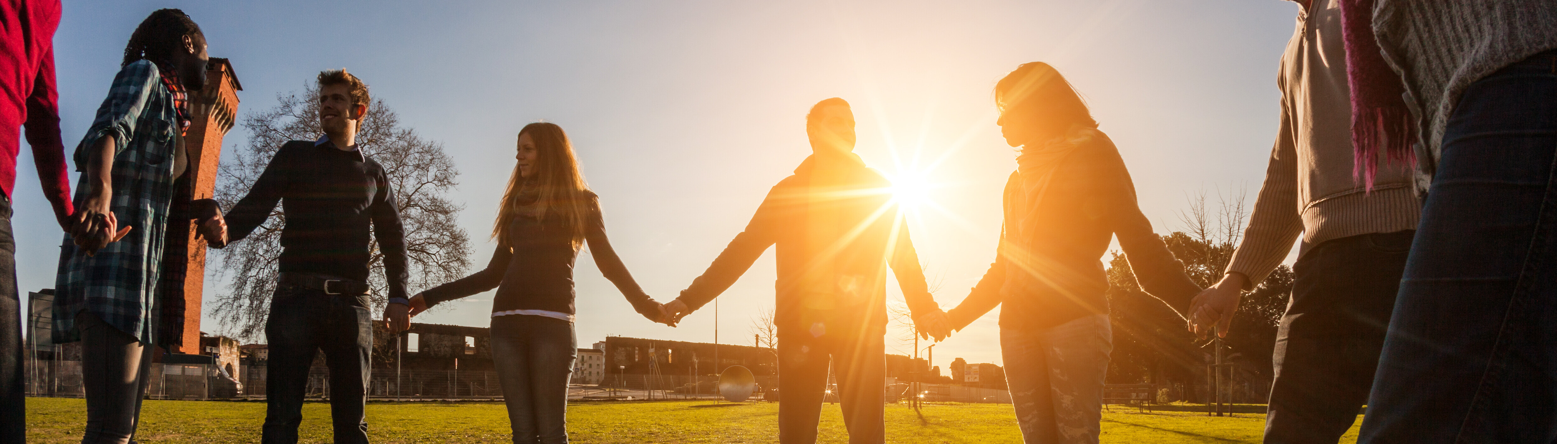 People standing in a circle holding hands at sunset