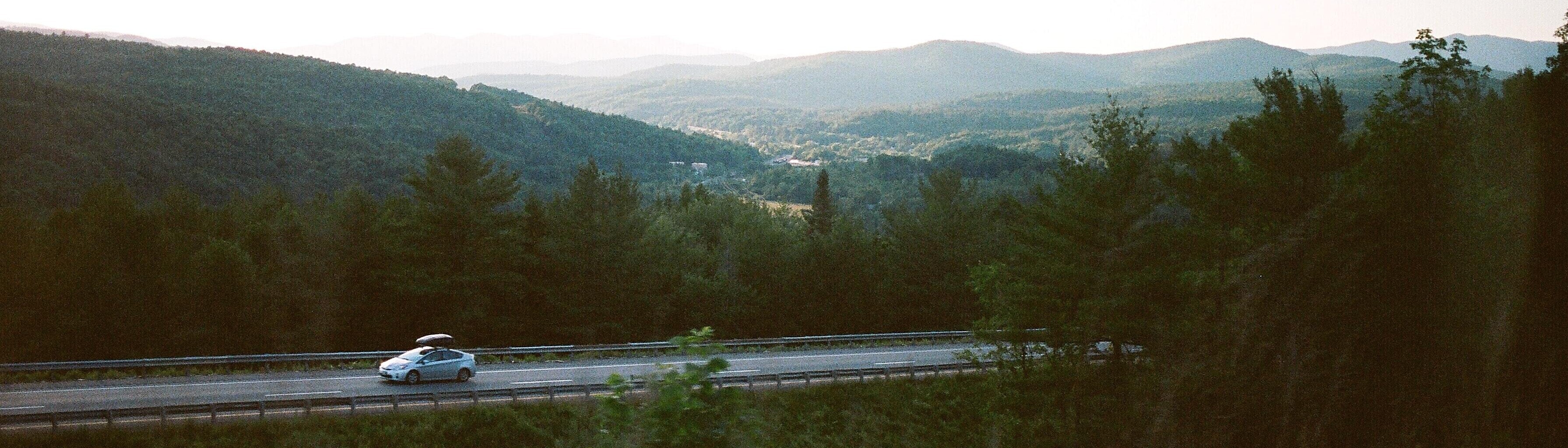 Green landscape background with a silver prius car driving on two lane road 