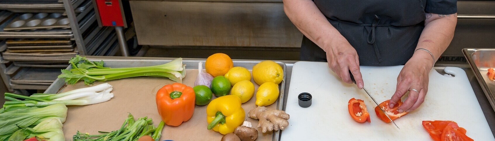 Hands chopping a pepper on a cutting board next to a sheet pan of colorful vegetables