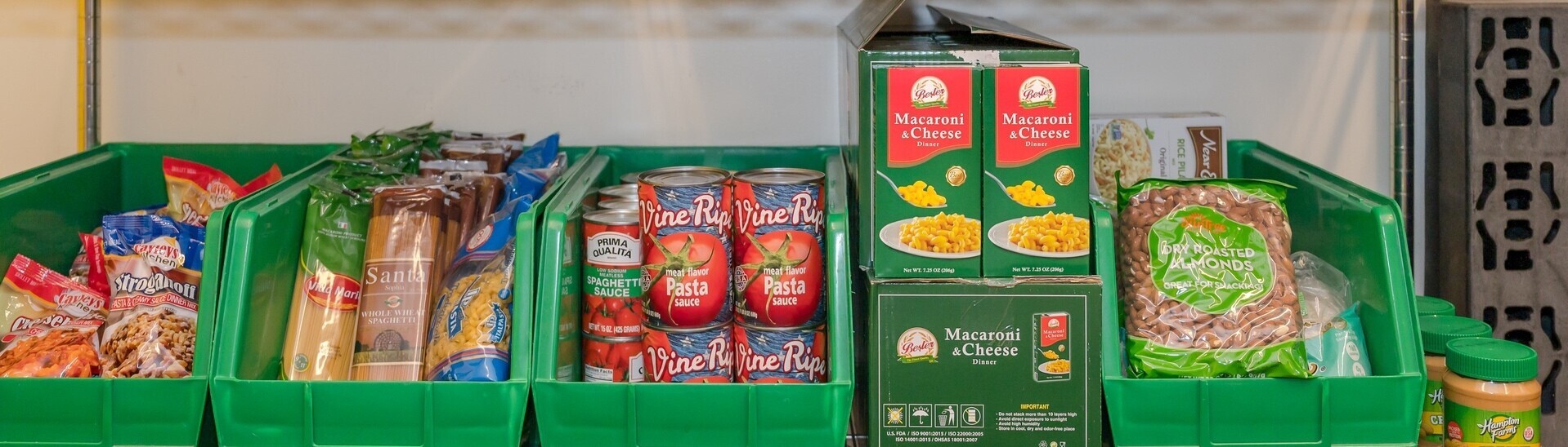 Green bins holding bagged stuffing, packaged pasta, canned sauce, boxed macaroni and cheese, and bagged nuts.