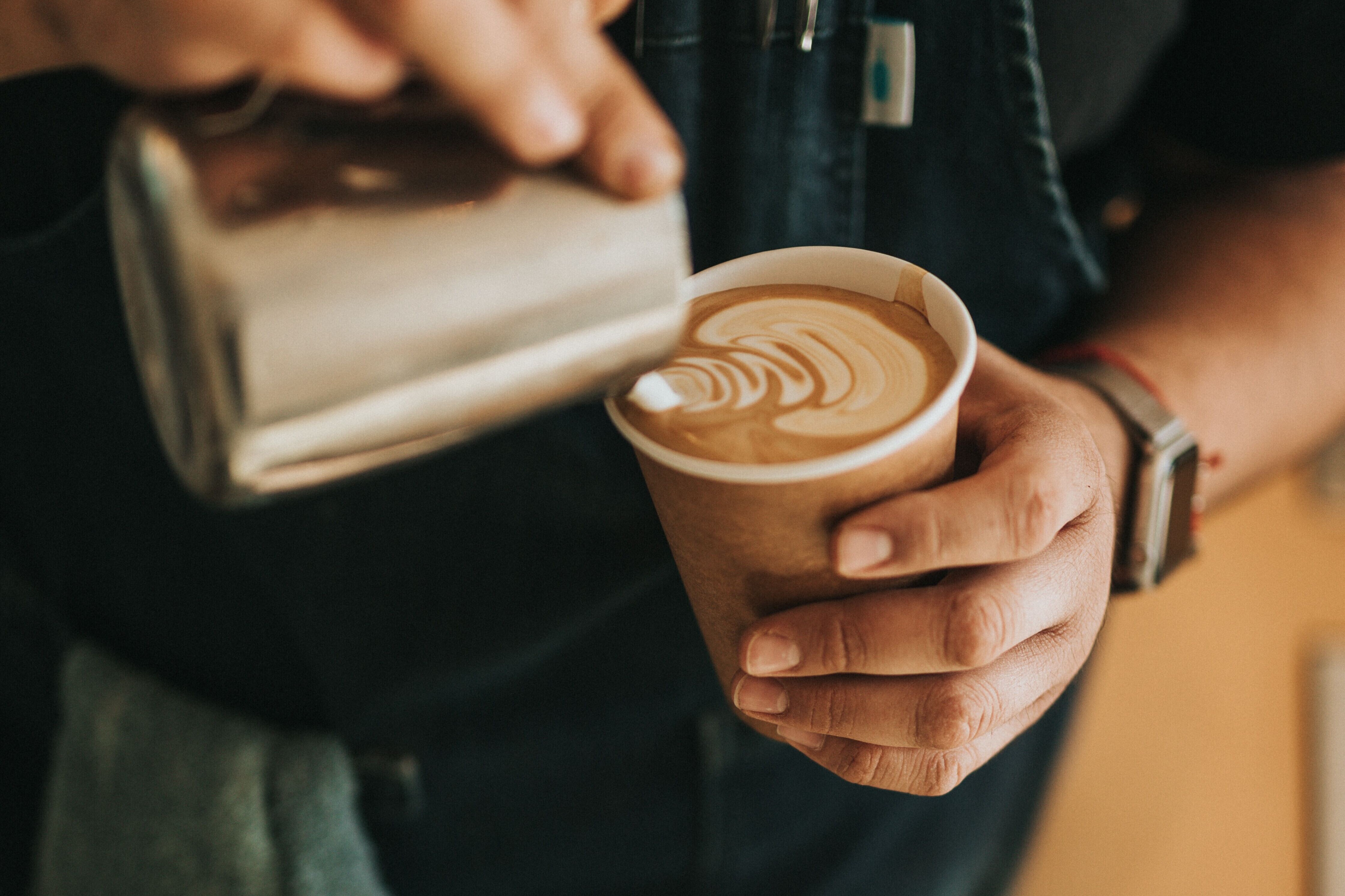 Hands of person holding a milk container being poured into a cup of coffee