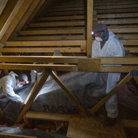 Workers in safety gear are installing insulation in an attic.
